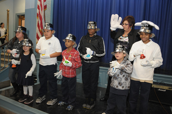 It’s all about shtick Dina Marks, the teacher behind the holiday concert — and the Mickey Mouse gloves — gets the bell ringers going at PS 63 in Ozone Park for “Auld Lange Syne.” (Miller photography)
