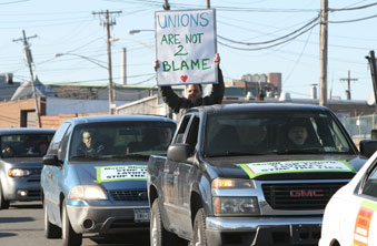 With signs fastened to cars and some held by members, vehicles are lined up as t