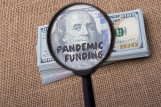Clipart image of a magnifying glass showing the words "pandemic funding" on a dollar bill