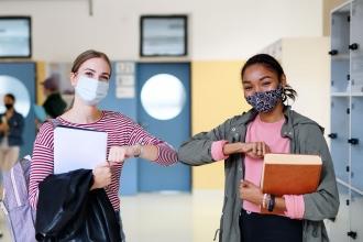 Two teachers wearing masks bump elbows instead of shaking hands. 