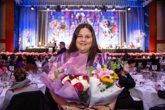 A woman smiles for the camera holding flowers after receiving an award. 
