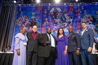 The Humanitarian Award winner at the 2024 Paraprofessional Festival and Awards Celebration stands on the stage with UFT leadership. 