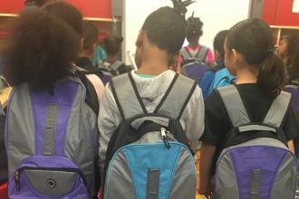 Image focuses on three students with backpacks on and their backs facing the camera
