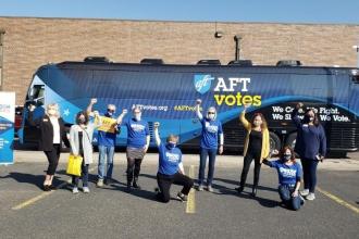 9 members raise their fists in front of a bus during their efforts to get out the vote