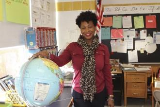 UFT model teacher standing in classroom with one hand on globe