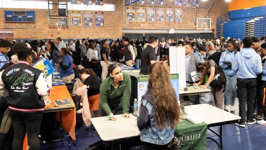 A large group of students roam a gymnasium at a college fair 