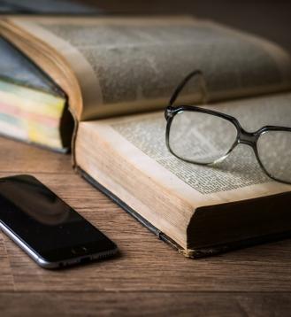Reading glasses on top of an old book, and a smart phone