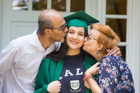 Teenager wearing graduation cap being kissed by two adults
