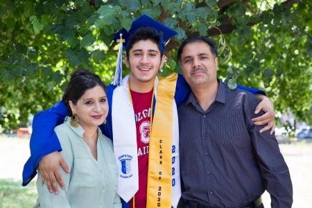 Teenager wearing graduation cap with his arm around two adults
