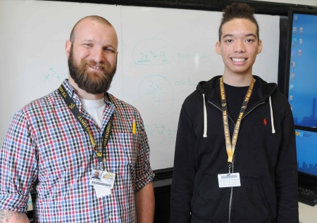 teacher with high school-aged student smiling in front of a whiteboard and computer