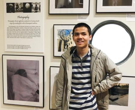 Roger Ng standing next to his photography on display 