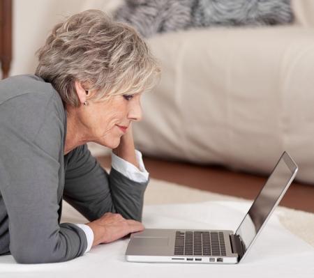 Mature woman laying on the floor looking at her laptop