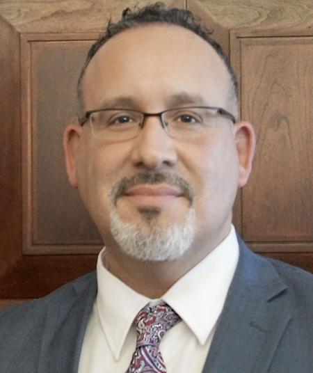 A headshot of Miguel Cardona