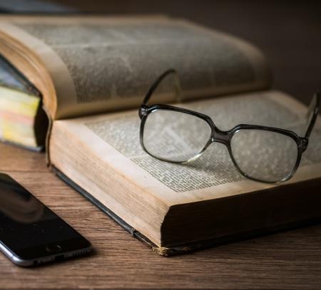 Reading glasses on top of an old book, and a smart phone