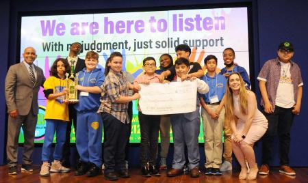 students stand on stage holding a trophy
