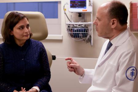 A man in a white lab coat speaking to a woman in a blue pattern shirt