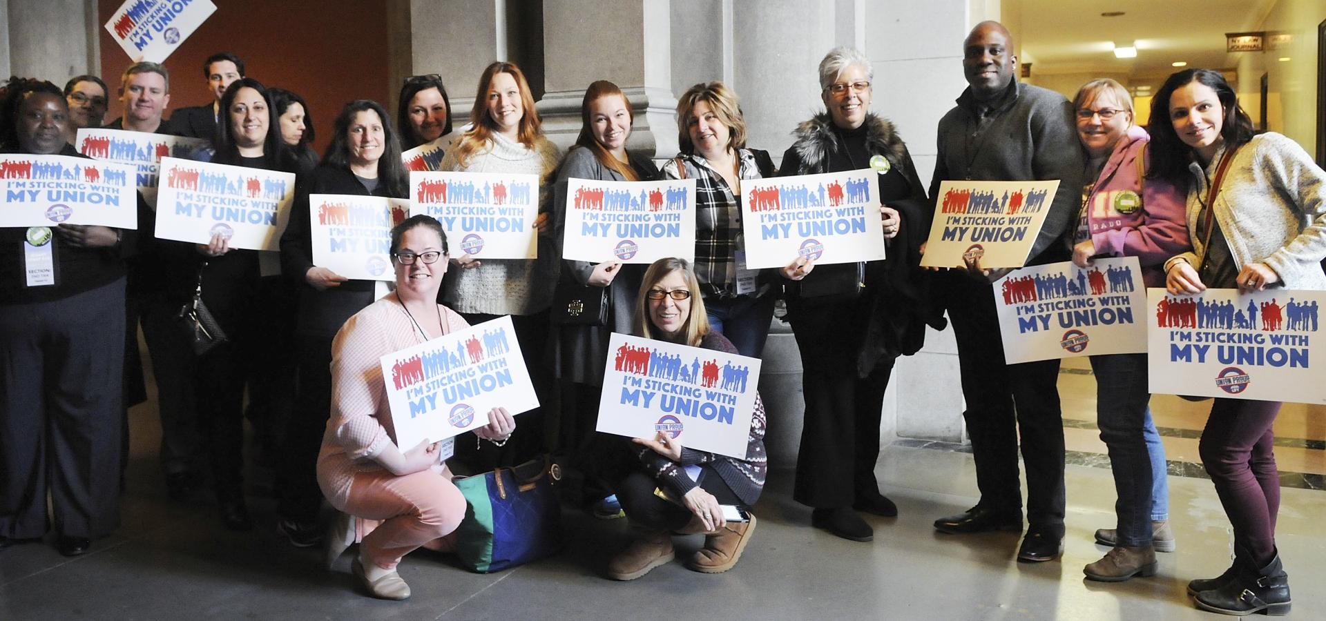 Group of people holding UFT signs that read "I'm Sticking With My Union"