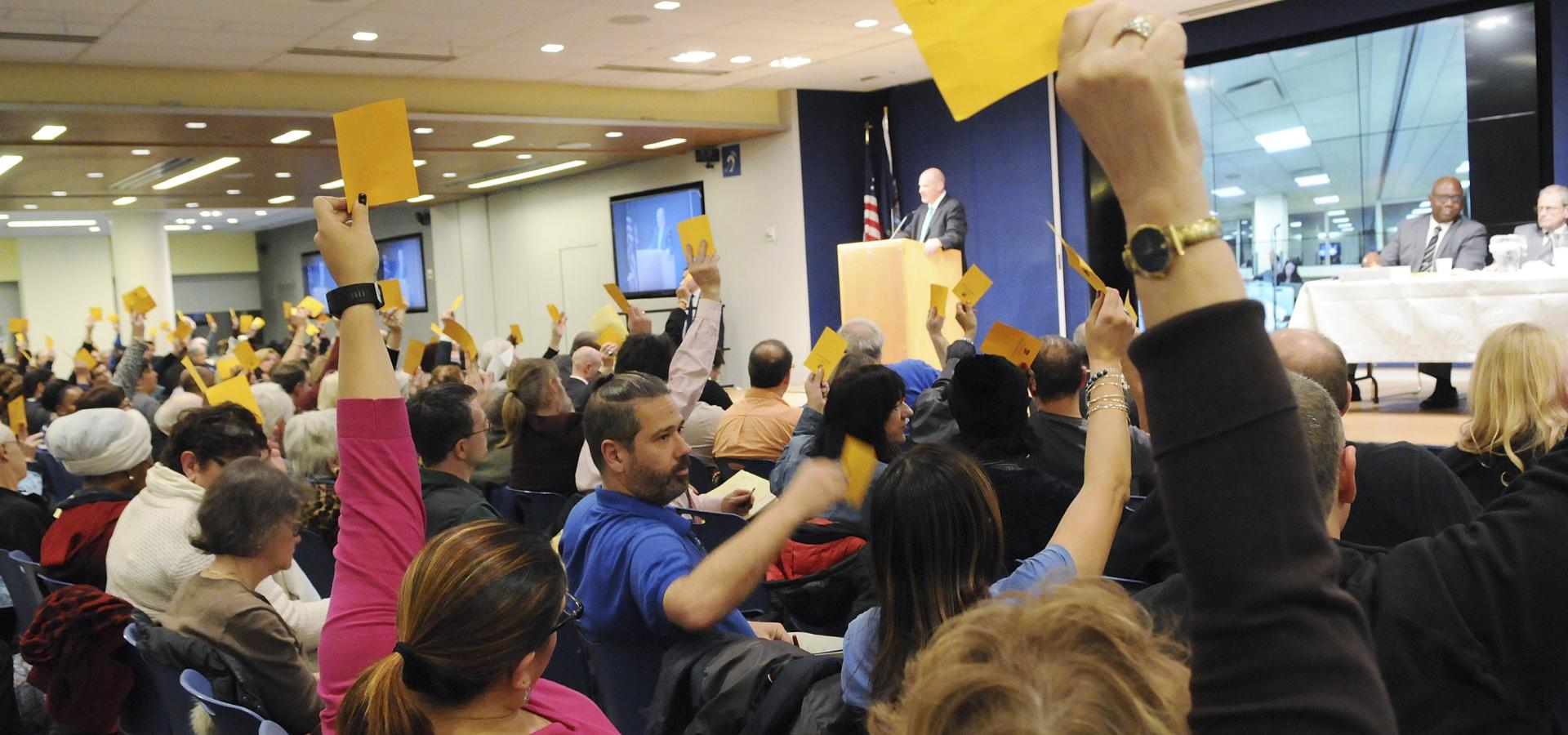 Crowd of seated people holding up yellow cards