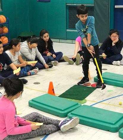 A 5th-grader at PS 22 putts on a miniature golf course, while his classmates awa