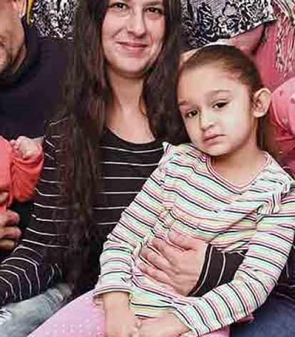 A group of 12 adults and 4 children smile in front of a decorated wall.