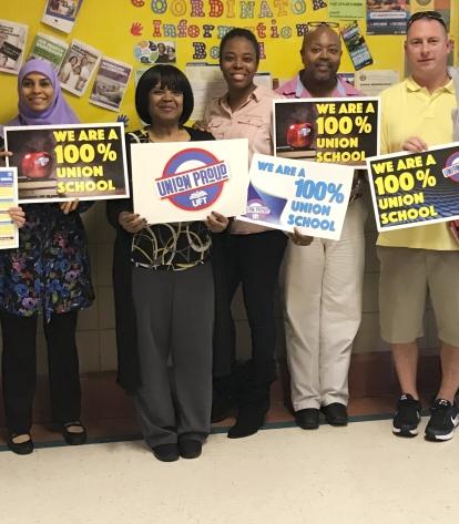 Group of diverse educators holding UFT signs that say "We are a 100% union school" and "Union Proud"