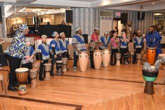 Kids dressed in traditional African clothing stand in a semi-circle behind drums