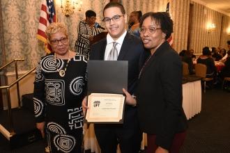 Man holding award smiles between two women 