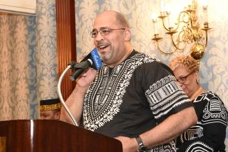 Man wearing a traditional African shirt stands at microphone behind podium