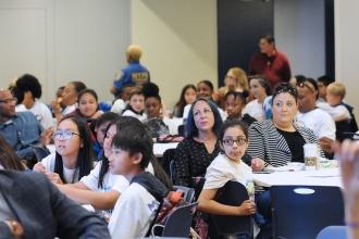 Kids and adults sitting at tables listening
