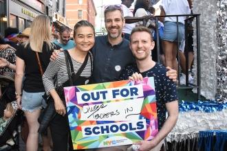 Three people pose with sign 'Out for Queer teachers in schools'