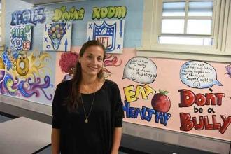 Melissa Neglia, the chapter leader at PS 21, stands with a mural provided by the