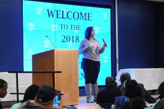 Woman on stage with big screen behinder her