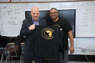 Two men pose for camera, one who is holding a school sweatsheet