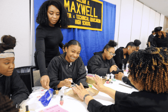 Women sitting at a long table receiving manicures by students