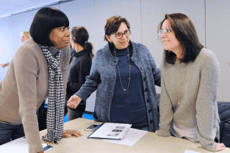 Three women talking while leaning over a table