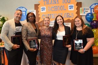 Four women and a man pose holding plaques