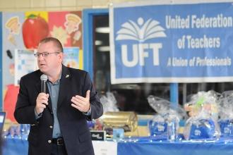 Micahel Reilly standing with a microphone with UFT banner and prizes behind