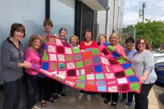 Women smiling showing off pink and multicolored crocheted blanket