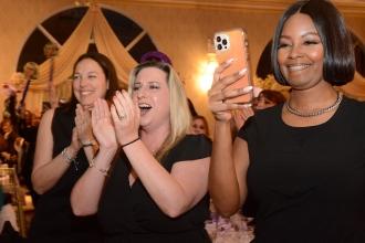 Three women applaud an award winner and one woman is filming. 
