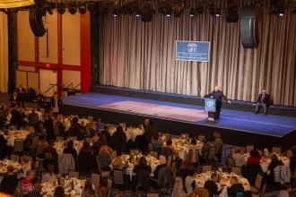 A man at the podium addresses a large crowd