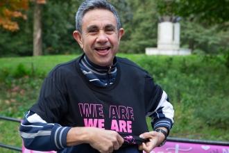 A man smiles while putting on a breast cancer awareness t-shirt