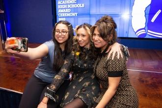 Three women sit at a stage and take a selfie