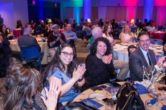 A group of attendees at a table clap in honor of an award winner 