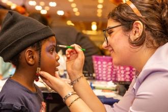 A high school student face paints a younger student's face