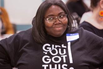 A woman smiles and is wearing a shirt saying "Girl you got this"