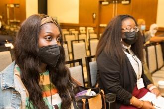 Two women wearing masks stare forward with intent 