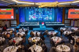 A man in a red shirt speaks to a large crowd 