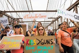 Members walking across the Brooklyn Bridge hold their signs in the air