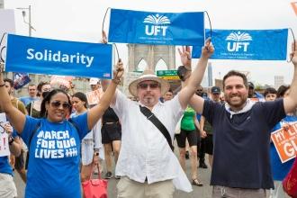 A group of UFT employees pose for a photo holding up their signs.