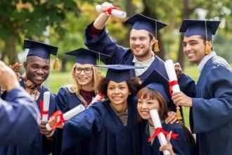 Students celebrating graduation pose for a picture wearing robes, caps and showing off their diplomas 